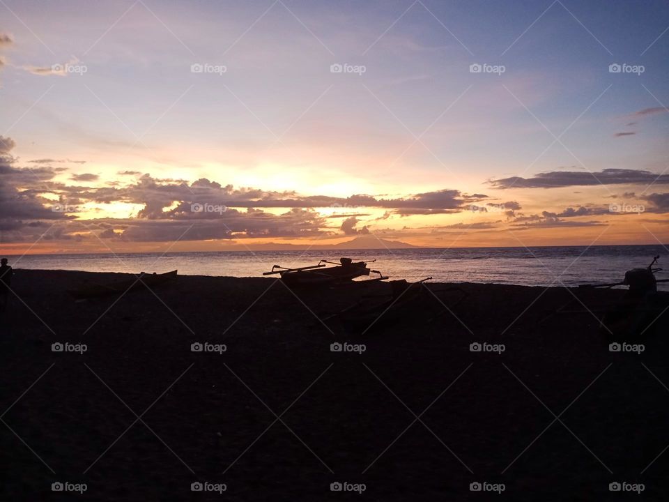 A fishing boat at the beach during sunset. Sun hidden by low clouds and different colors in the sky