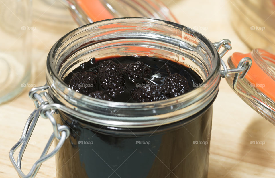 A close up view of homemade mulberries in syrup preserved in a glass jar.