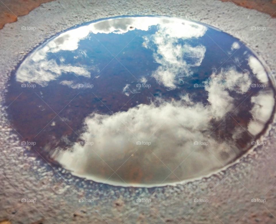 an old plough disc with water in it showing the reflection of the sky