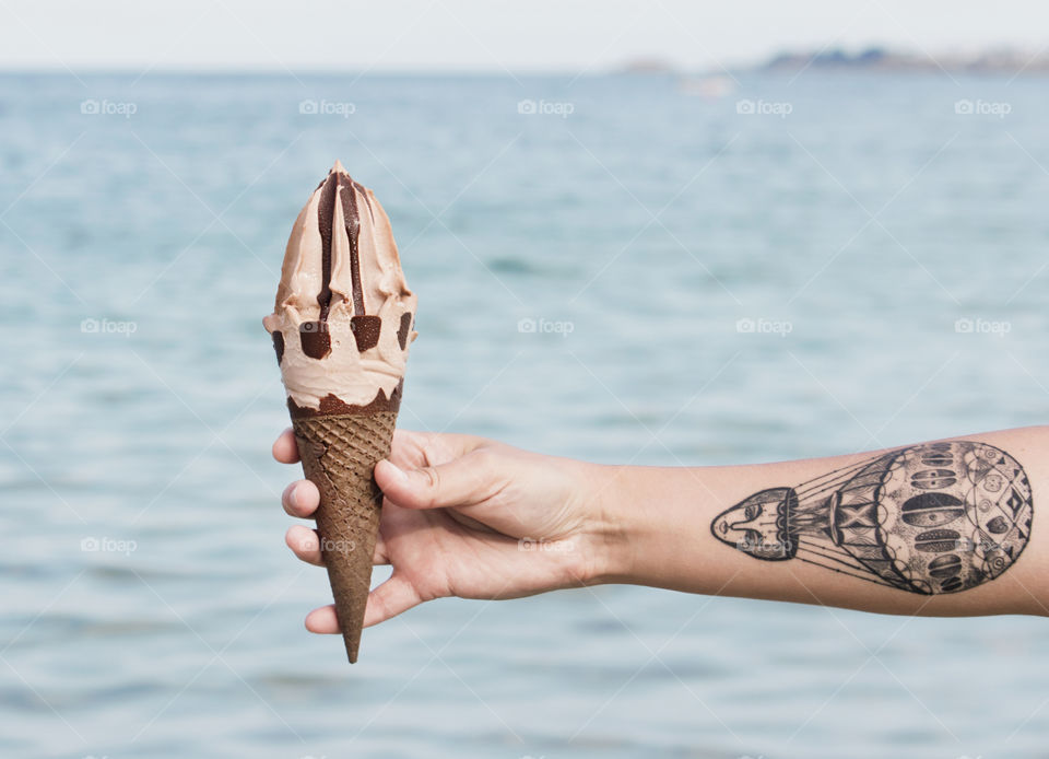 A hand with tattoo holds an ice cream at the sea background