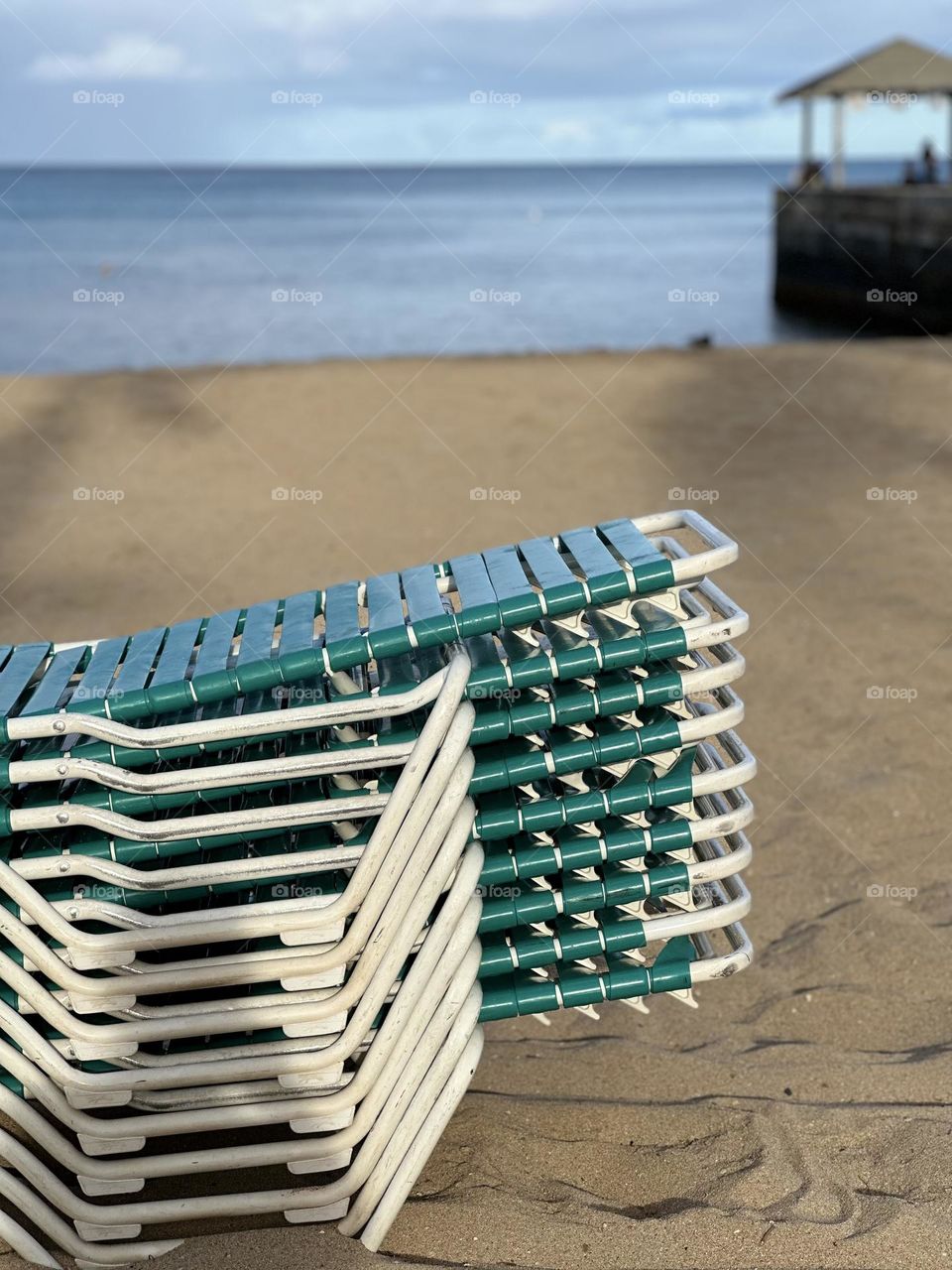 Stack of green and white beach chaise lounge on the sand with the end-of-the-pier gazebo in the background 