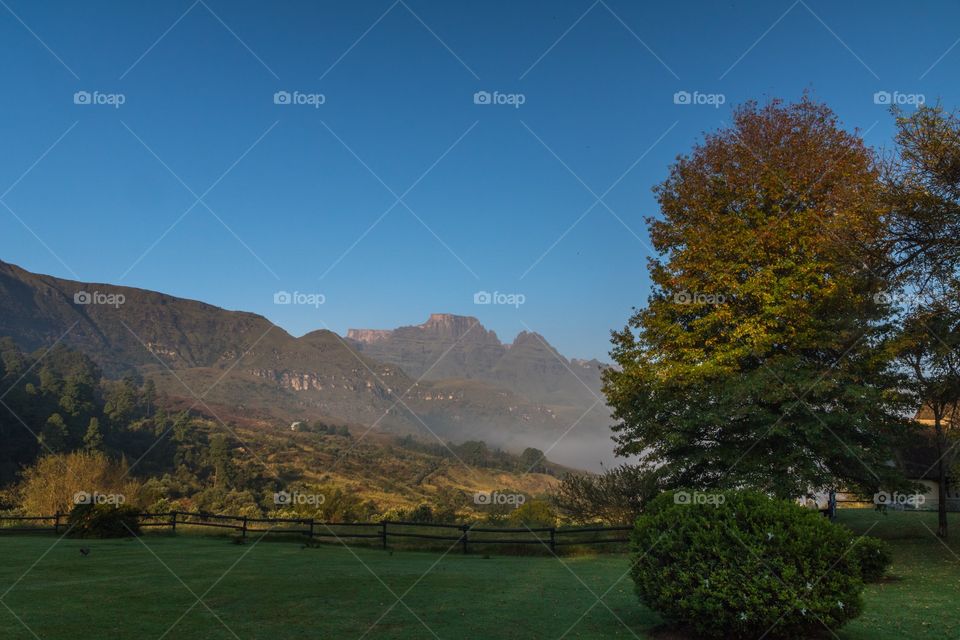 Early morning mountain range with fall colored trees, blue sky and foggy settling over the valley