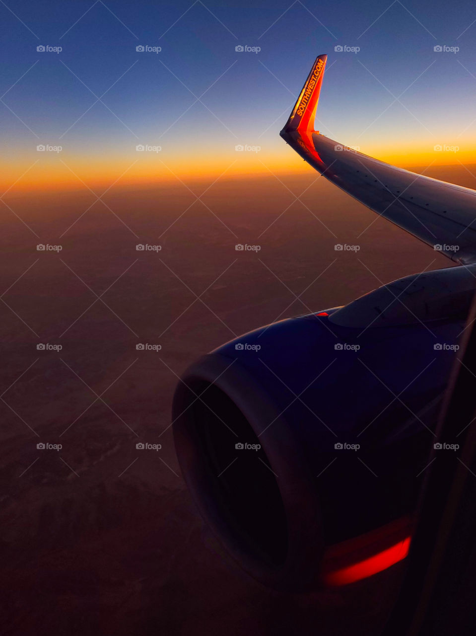 An aircraft winglet and the horizon share the same colors as the sun sets