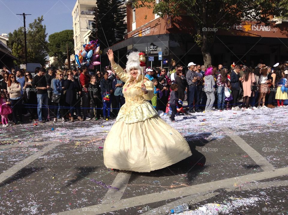 Man dressed as a woman waving to the crowd in a carnival parade.