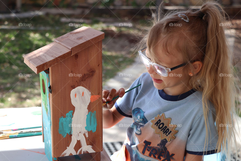 Child painting a wooden bird house