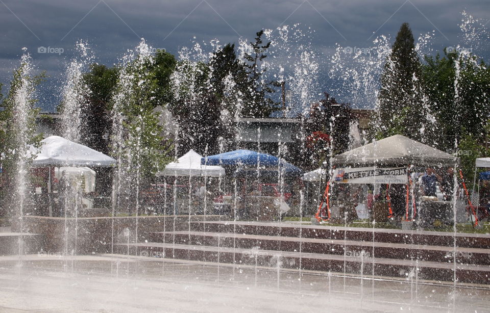 A beautiful fountain at Centennial Park in Redmond in Central Oregon contrasts against a stormy gray sky on a summer afternoon. 