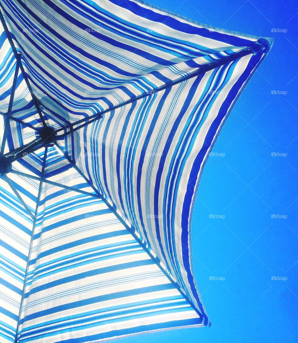 Looking up at blue and white striped beach umbrella with summer blue sky in the background. 