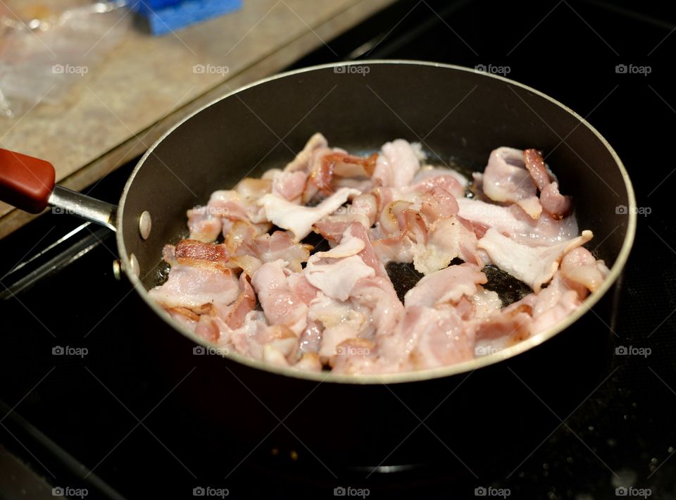 Fresh pork bacon in a hot frying pan on a stove