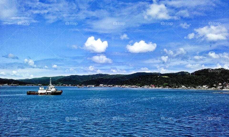 Thug boat navigating in a calm crystal clear blue water with beautiful blue skies.