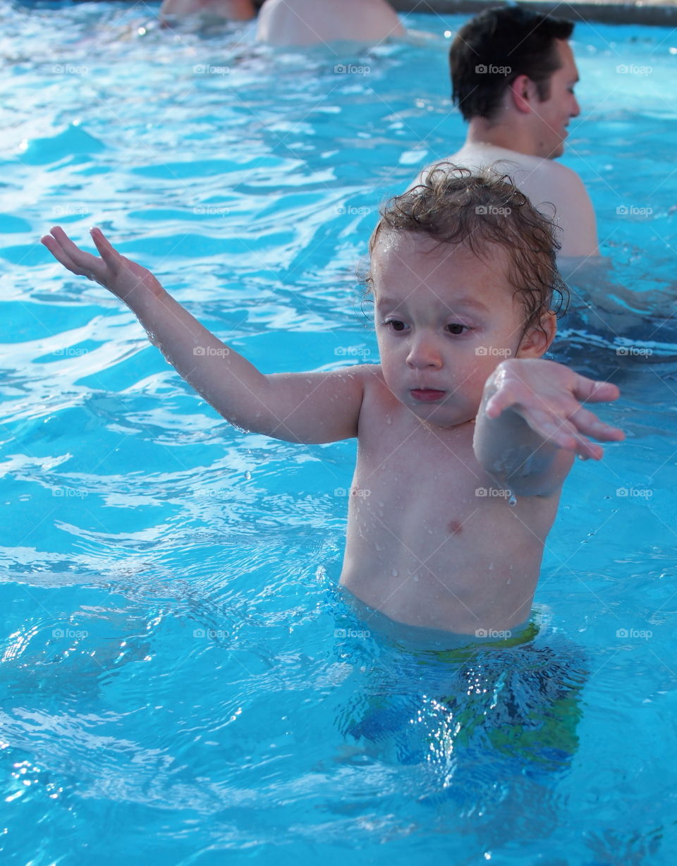 A small boy having lots of fun playing and cooling down in an outdoor pool on a hot summer day. 