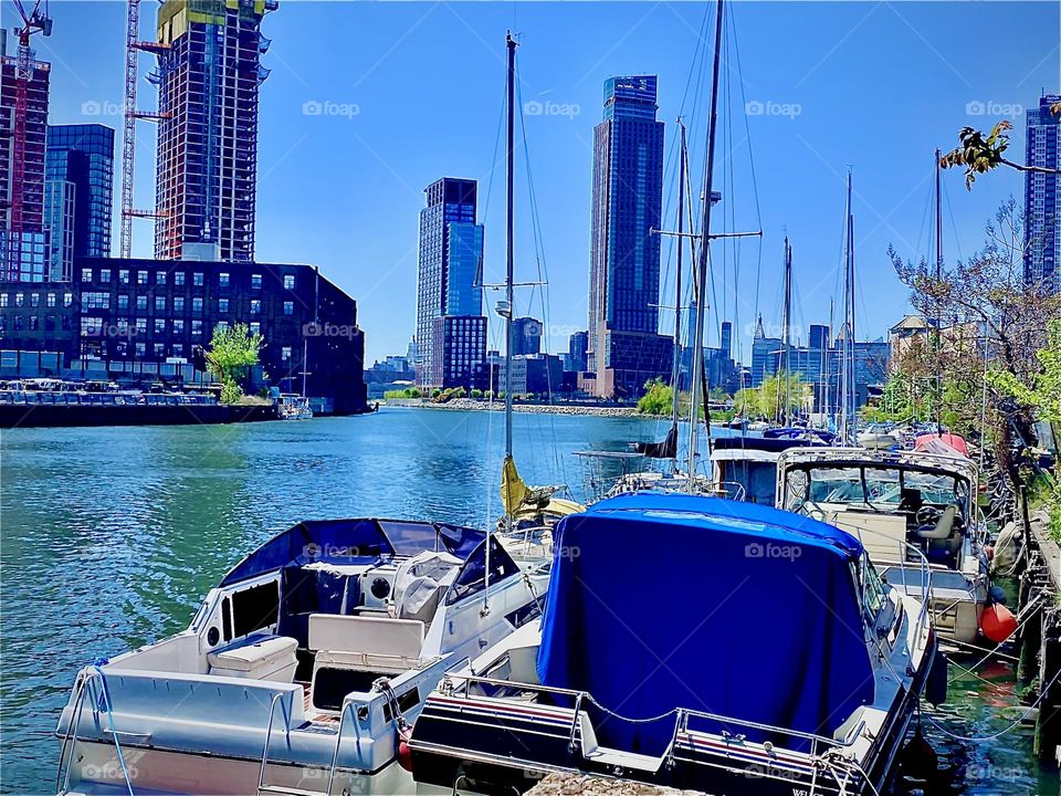 An overview of the „Newtown Creek“ boat area with its various different picturesque boats and across the East River you see Greenpoint, Bklyn on the right and the LIC, Queens and also the Manhattan skyline on the left. 2022. Hypnotic Productions
