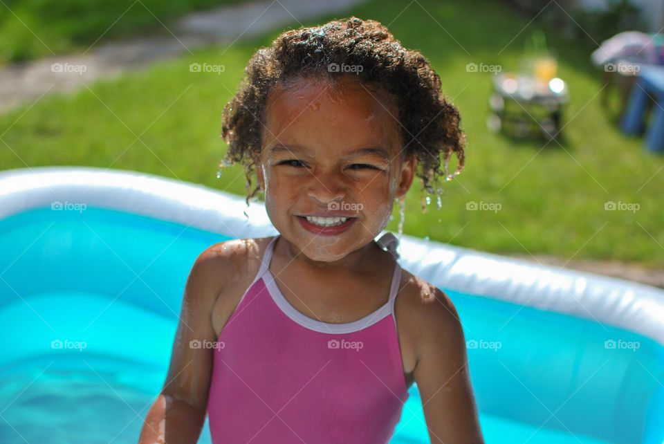 Cute little girl enjoying some playtime in a swimming pool during a hot summer day, looking for refreshment