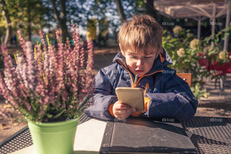 Boy with smartphone outside. Boy looking on a large smart phone, outdoors at table