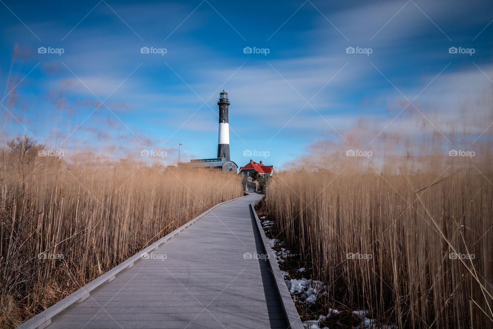 Path to a lighthouse with lots of moving clouds streaking across the sky. 