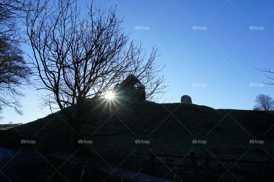 Catching Sunbeams .... sun peeping out behind a ruin ... photo taken with a backdrop of a clear blue sky 