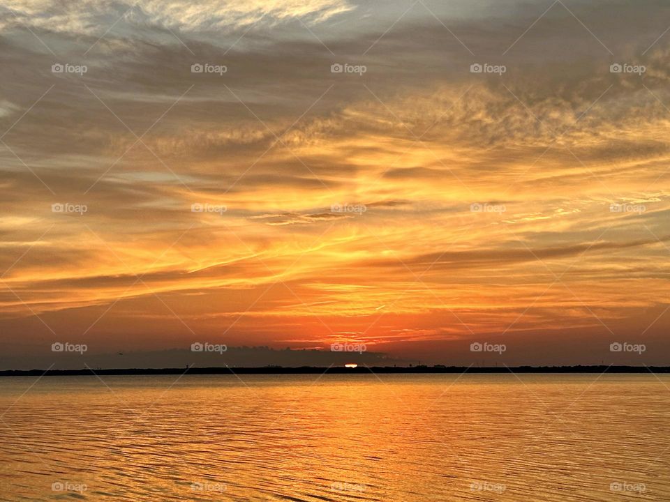 The golden disc is already touching the surface of the ocean. It seems in a hurry to disappear, slipping quickly behind the line of the horizon spreading its last rays.