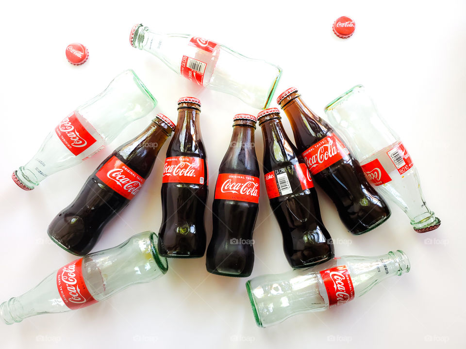 Small Coca-Cola bottles both new and consumed on a white background.