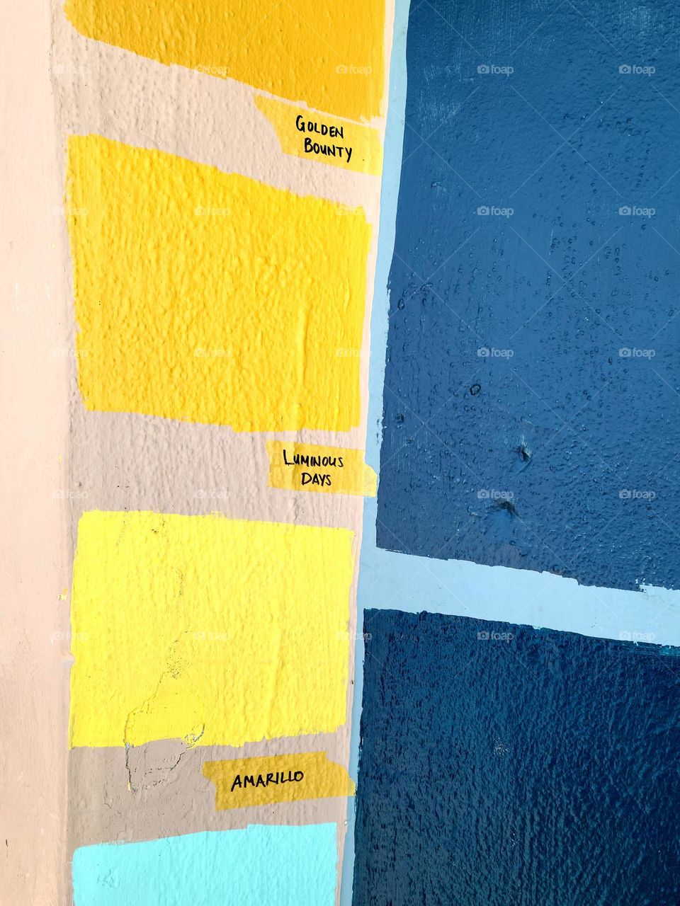 Different colored paint samples painted onto a stucco wall, shades of yellow and blue