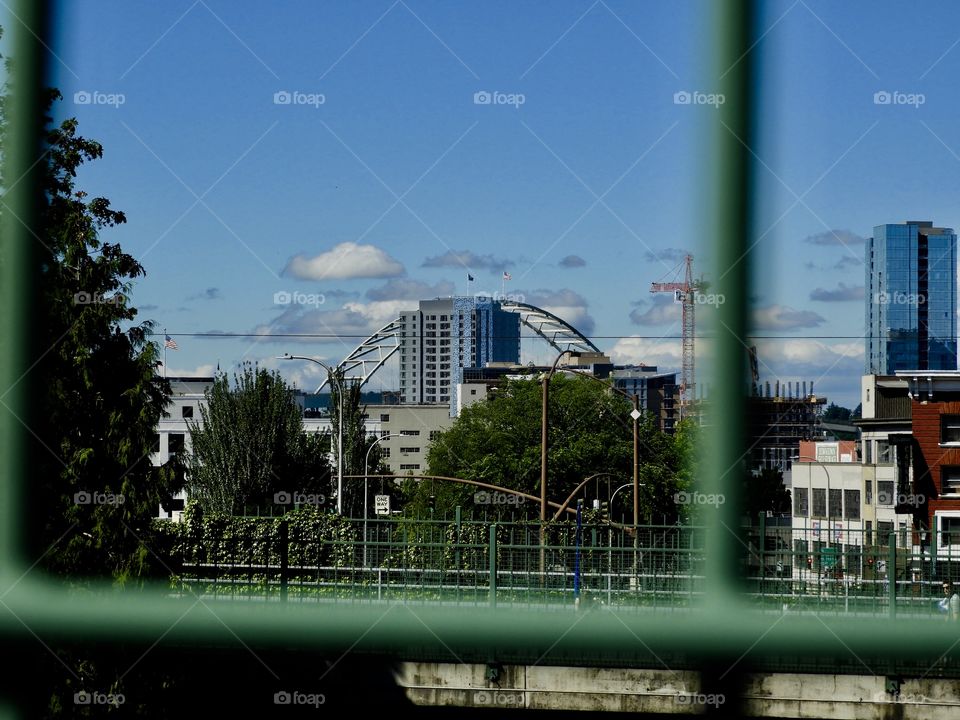 City peeking through the wrought iron fence. The blue sky with a thin lining of cute puffy clouds makes the building and the Fremont bridge pop. 
