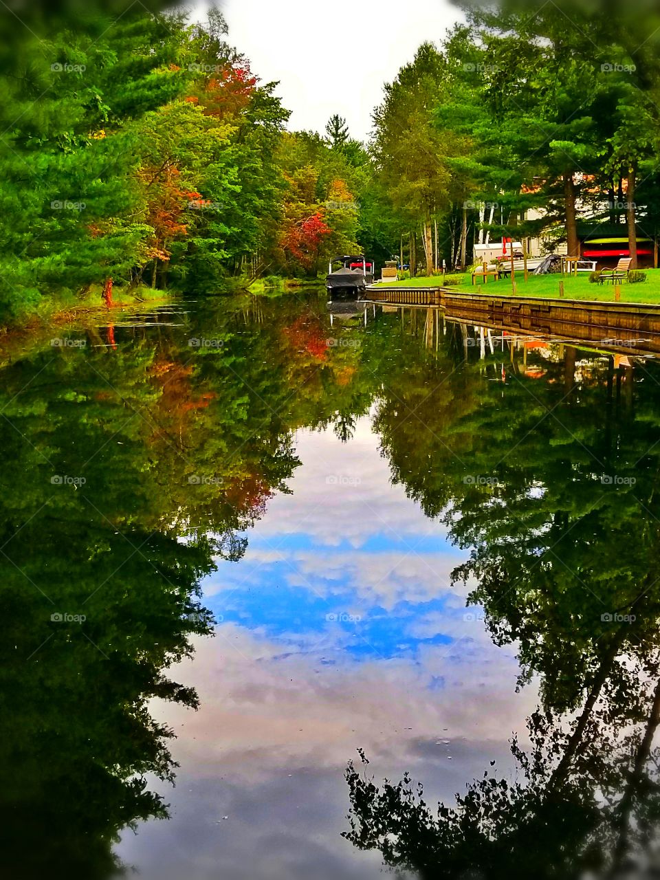 Beautiful reflection off the water, looks like a painting. The blue sky and trees looks like they're looking at a mirror.