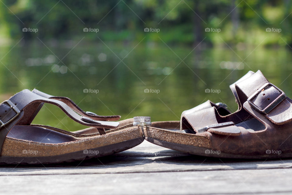 Wedding rings sit on top of a pair of sandals on a dock at the lake