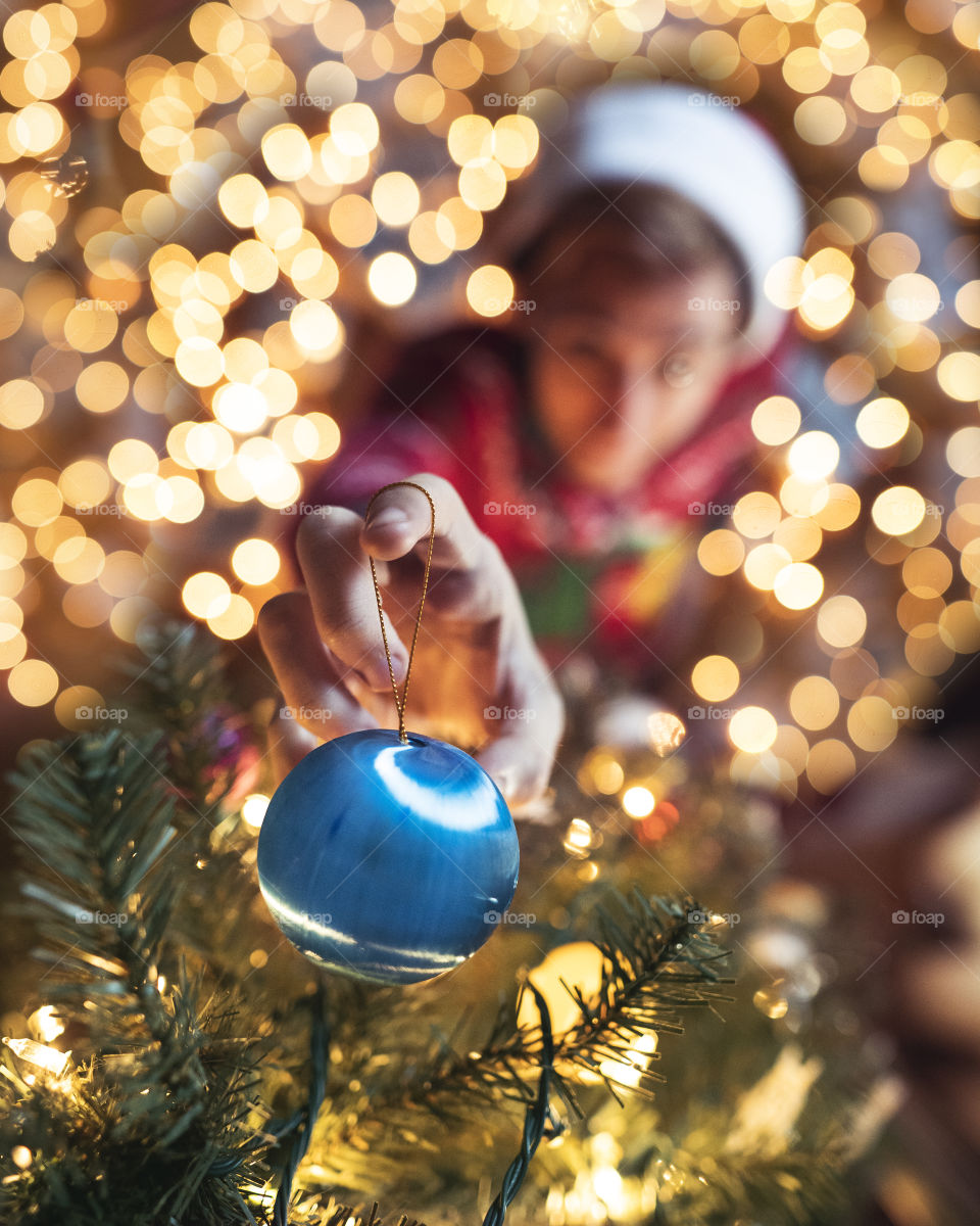 A man in a Santa hat and sweater decorating the Christmas tree with ornaments for the holiday season to be festive with lights