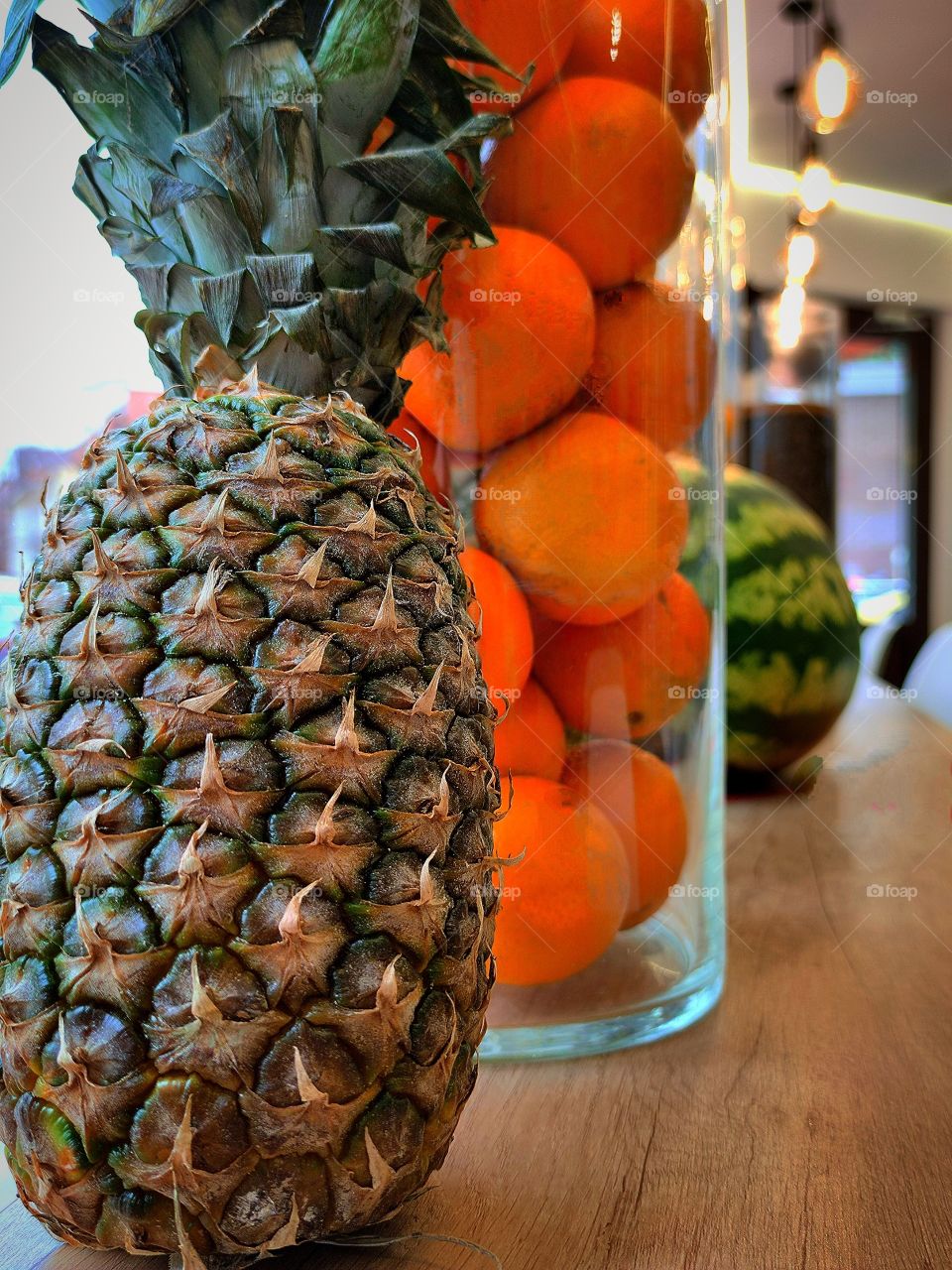 Fruit mix.  A pineapple.  A jar of oranges.  watermelon along the rack