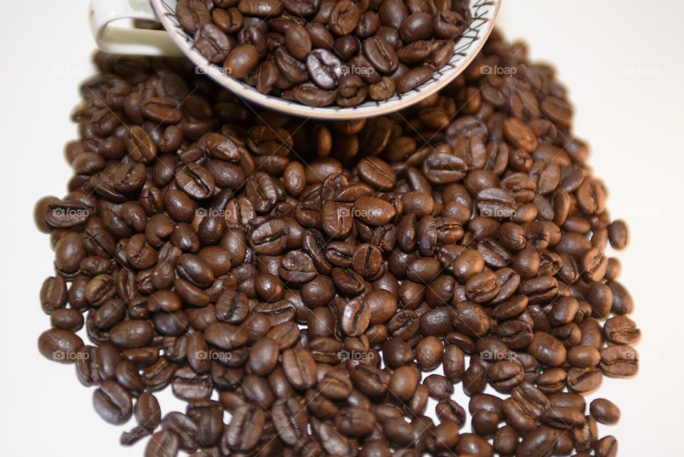Aromatic coffee beans in a white cup on a white background. Roasted coffee beans close up.
