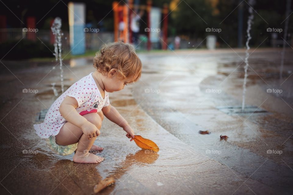 Baby girl playing with leaf in puddle