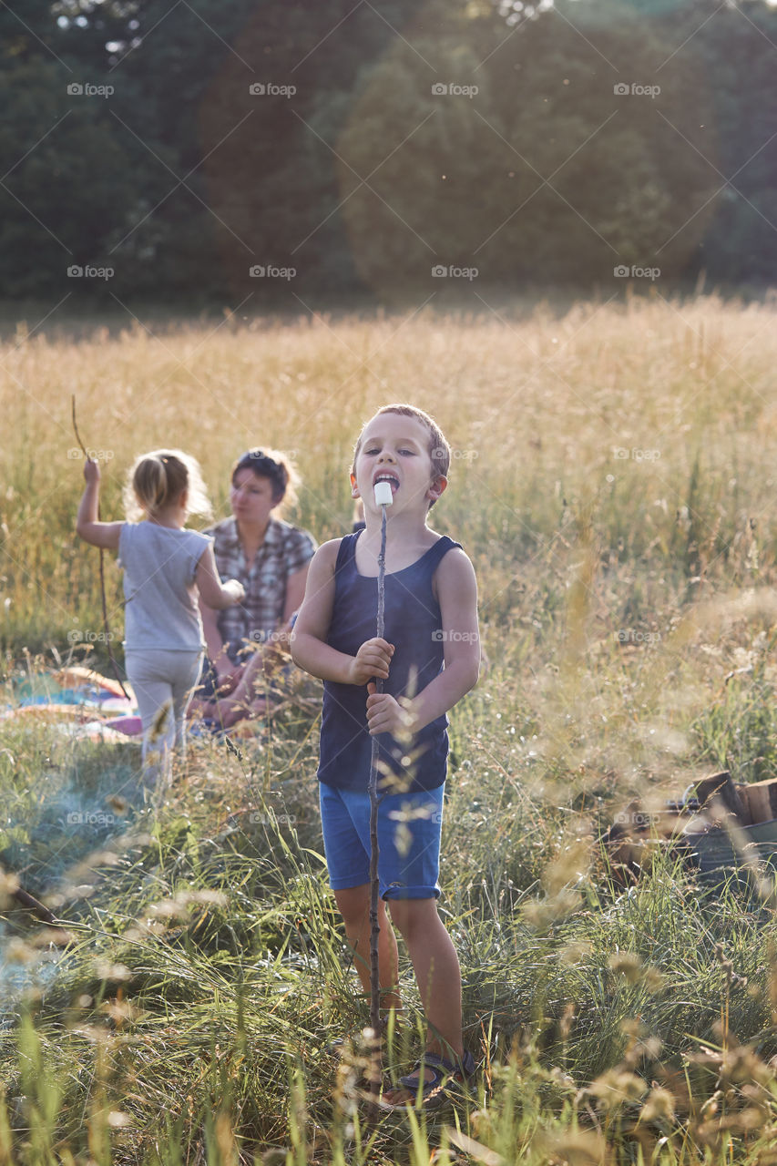 Little boy eating a marshmallow after roasting it over a campfire on a meadow. Candid people, real moments, authentic situations