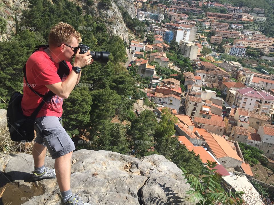 Male tourist taking picture of the town Cefalu high up on a mountain on Sicily.