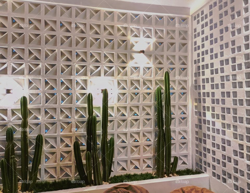 Modern minimalistic and bright living room in shades of dark white with bean bag chair, two coffee tables with carpet and cactuses on background and textured wall.