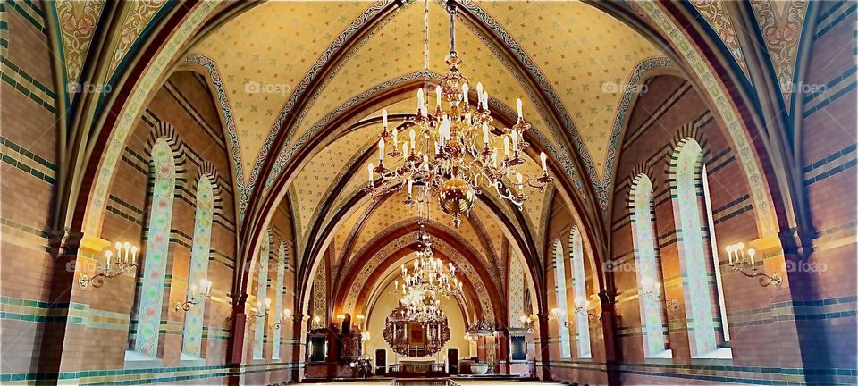This is the interior of the cathedral in “Trelleborg”, “Sweden” by the “Baltic Sea”. The inter angled pointed arches by the ceiling section off either areas with multiple tall windows or a hallway or through way. 2023. Hypnotic Productions
