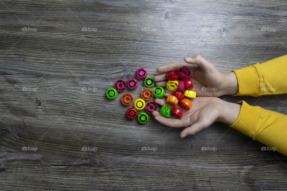 We collect garbage, plastic plugs and plastic to save our planet, nature and the environment. Men's hands lie on a gray wooden surface, which is used as a background or a surface with incident light.