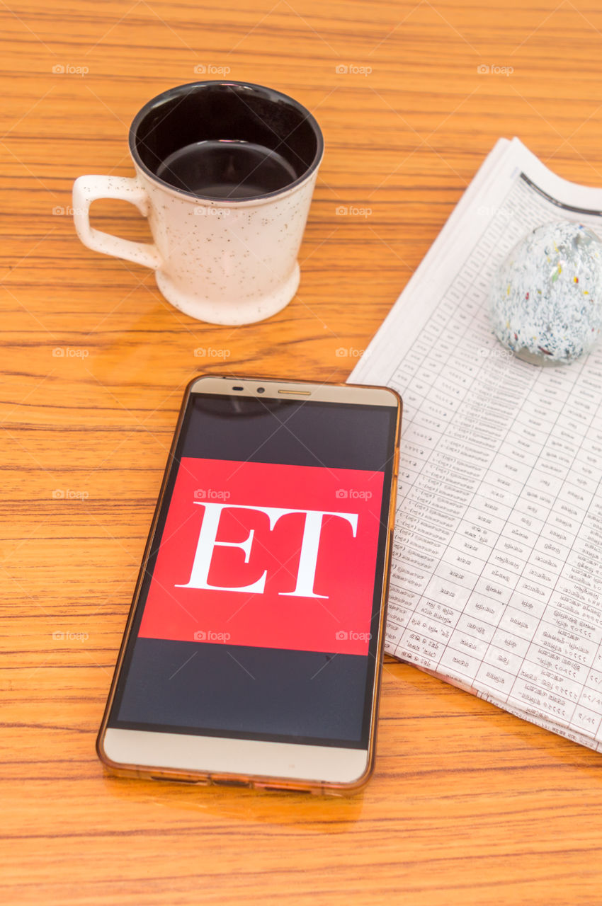 Kolkata, India, February 3, 2019: Economic Times (ET) news app visible on mobile phone screen beautifully placed over a wooden table with a newspaper and a cup of coffee. A Technology Product Shoot.