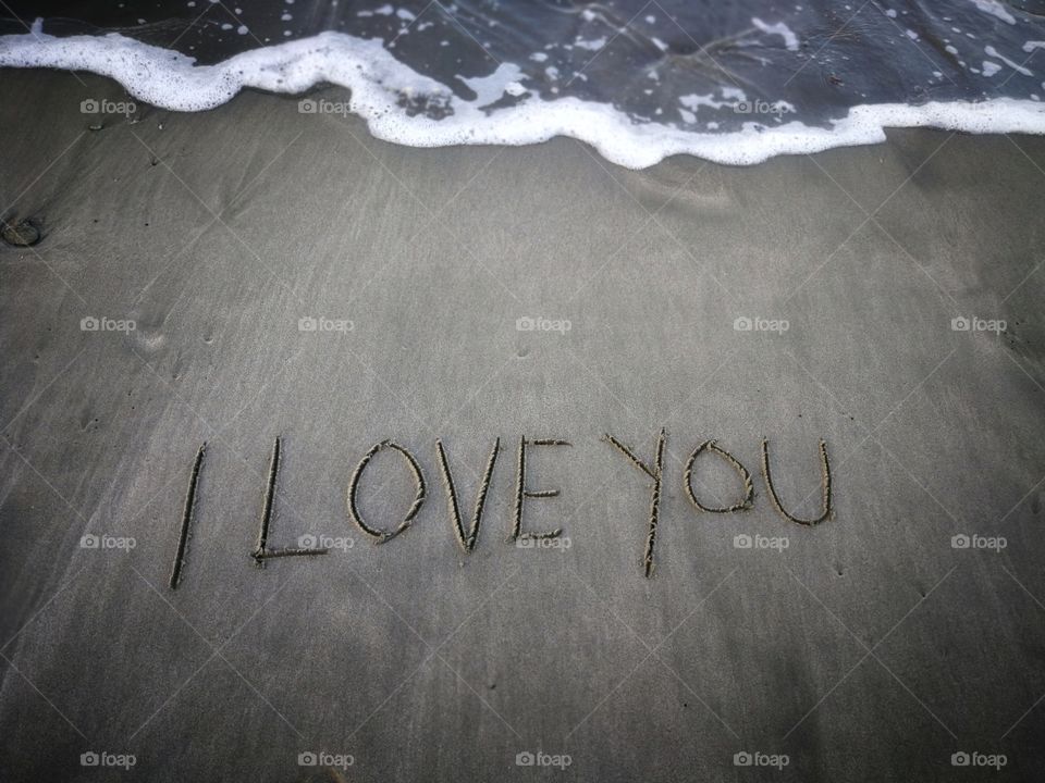 Word "i love you" outline on the wet sand with the wave brililliance.