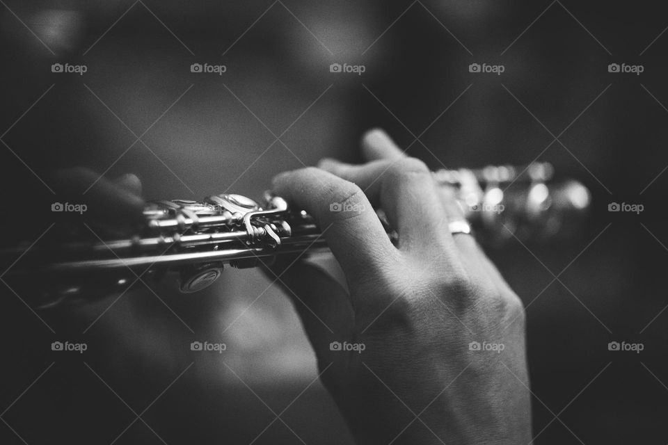 A portrait of the fingers of a flutist placed on the valves of a silver flute to produce a beautiful sound.