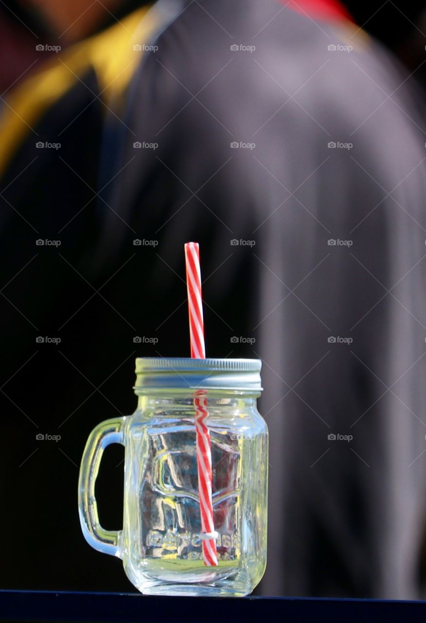 Mason jar glass mug with red and white striped straw closeup outdoors