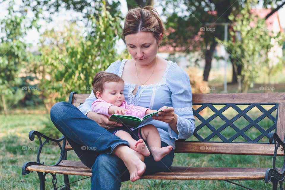 Mom and daughter sitting on a park bench and reading book