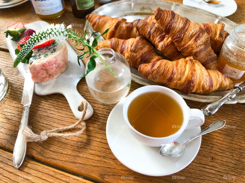 Breakfast with croissants, tea, jam, cheese, strawberries, flower in a vase