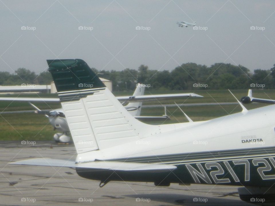 Small planes at airport and one plane up in the air after take off