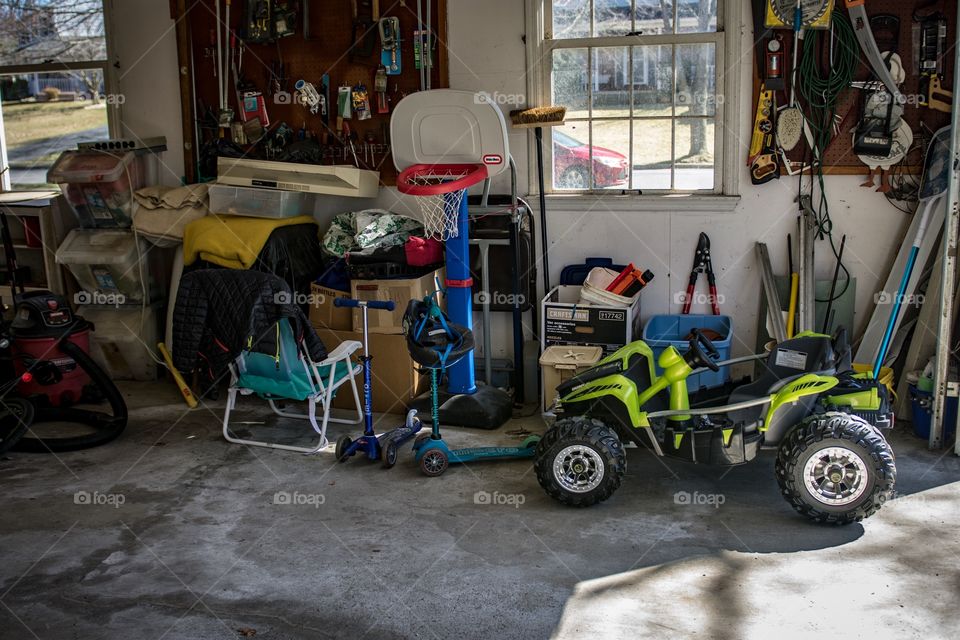 Four wheeler roadster parked in garage next to mini basketball playlet, tools on wall, patio furniture and various other run of the mill accrued junk a normal suburban garage would have in it on a beautiful spring day.