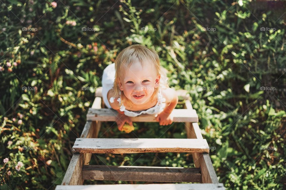 Cute blonde toddler little girl climbs up the ladder, country side, cottagecor