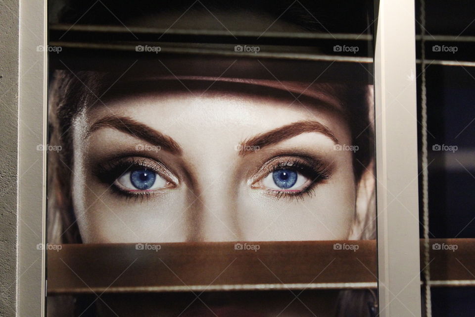 blue eyes looking through the blinds of a window