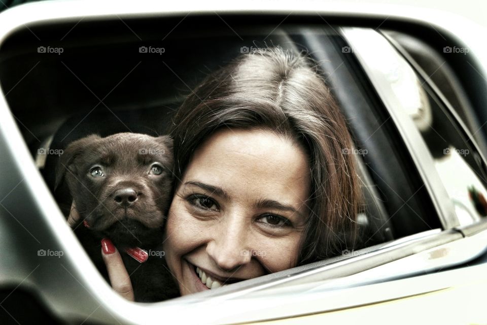Reflection of woman with her puppy on side mirror