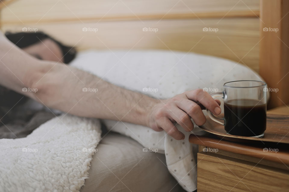 Man in bed grabbing a cup of coffee.