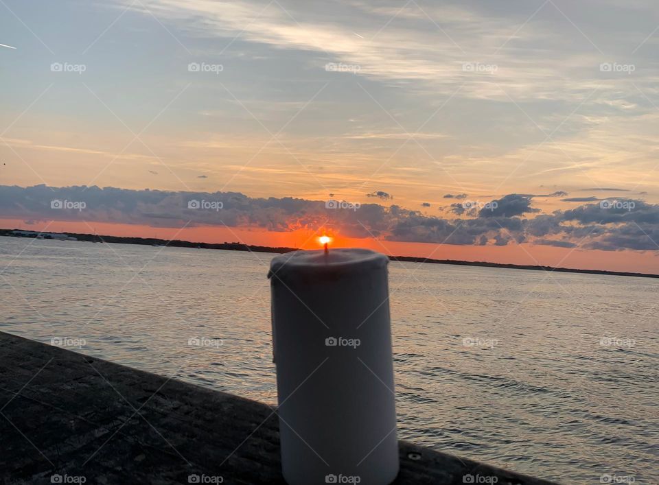 Candle Seems To Be Lit Up With A Small Flame From The Sun Setting By The Water In The Horizon.