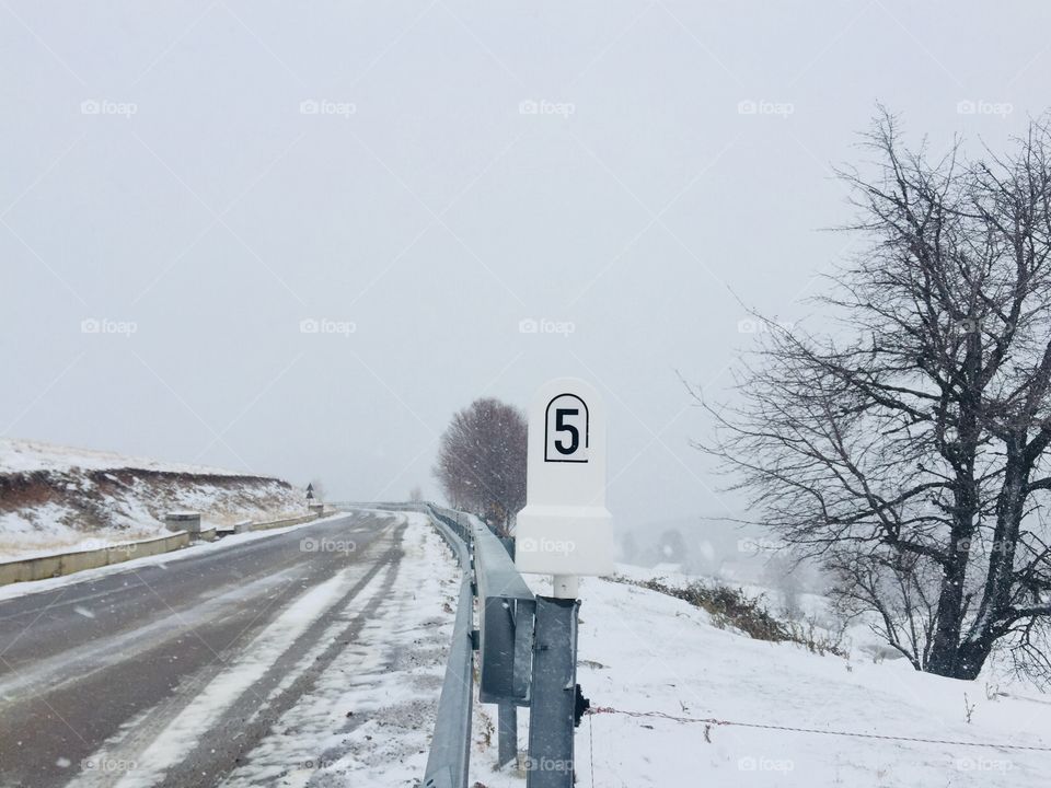 Stone mileage sign on a deserted road covered in snow during winter