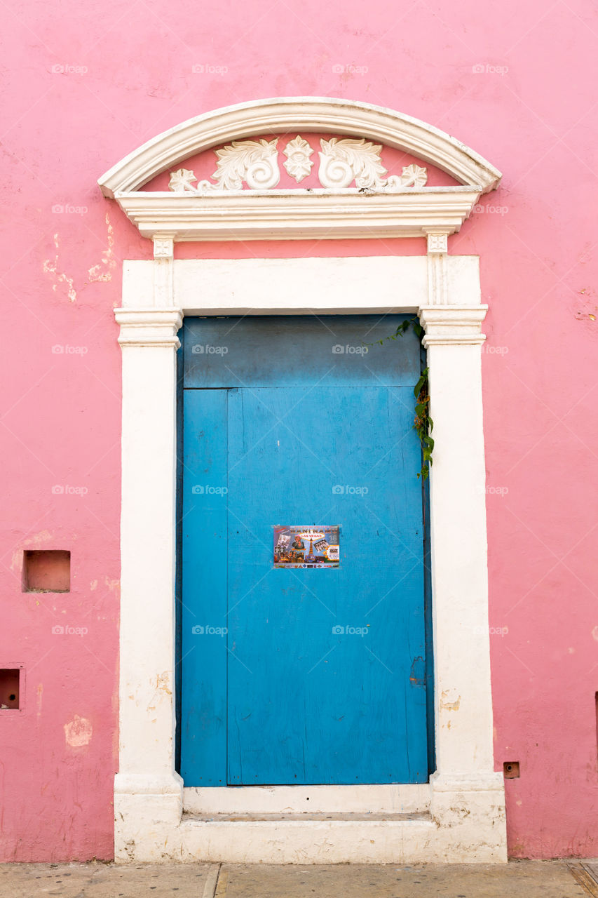 Blue door on a pink building. Deep blue colored door in a pink wall. Colorful building. White decoration close to the door