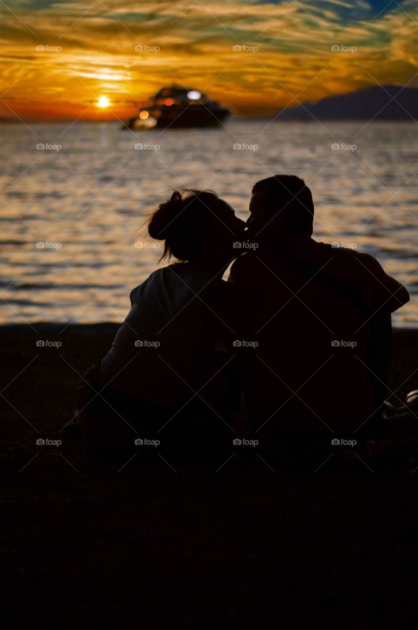 Couple sitting on the beach and enjoying romantic sunset